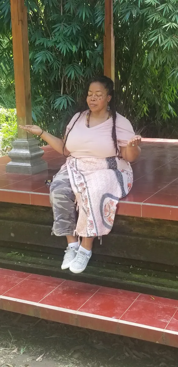 Cheri meditating, palms open, in a garden pavilion