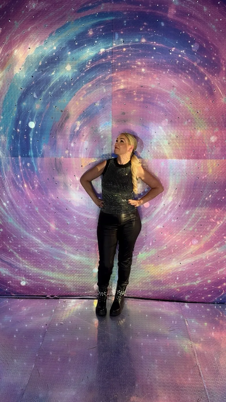 Jaclyn standing hands on hips in front of a swirling galaxy portal, looking up